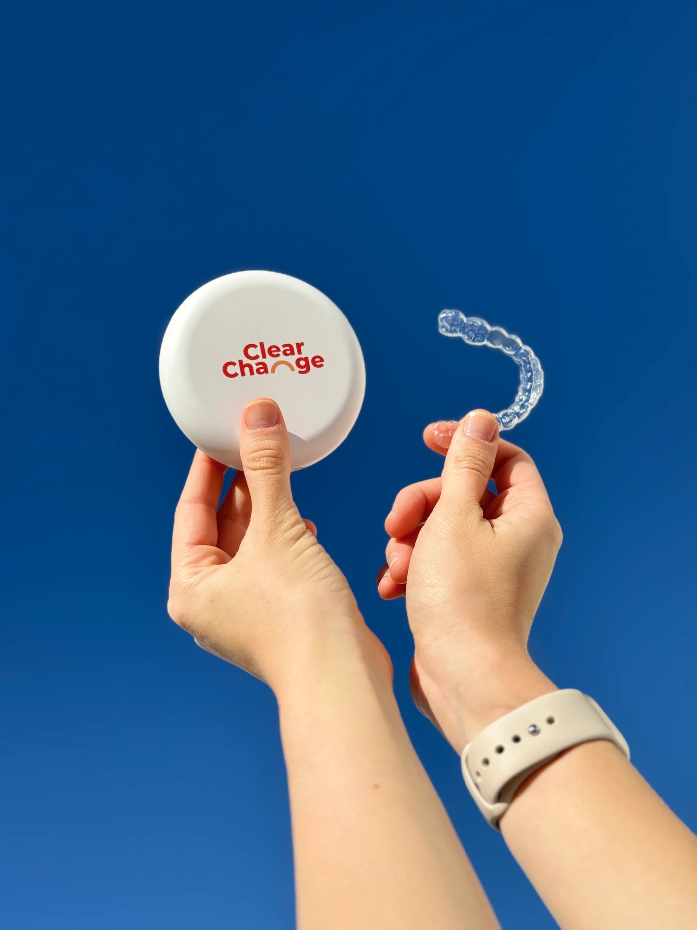 ClearChange aligner and branded case held against a blue sky